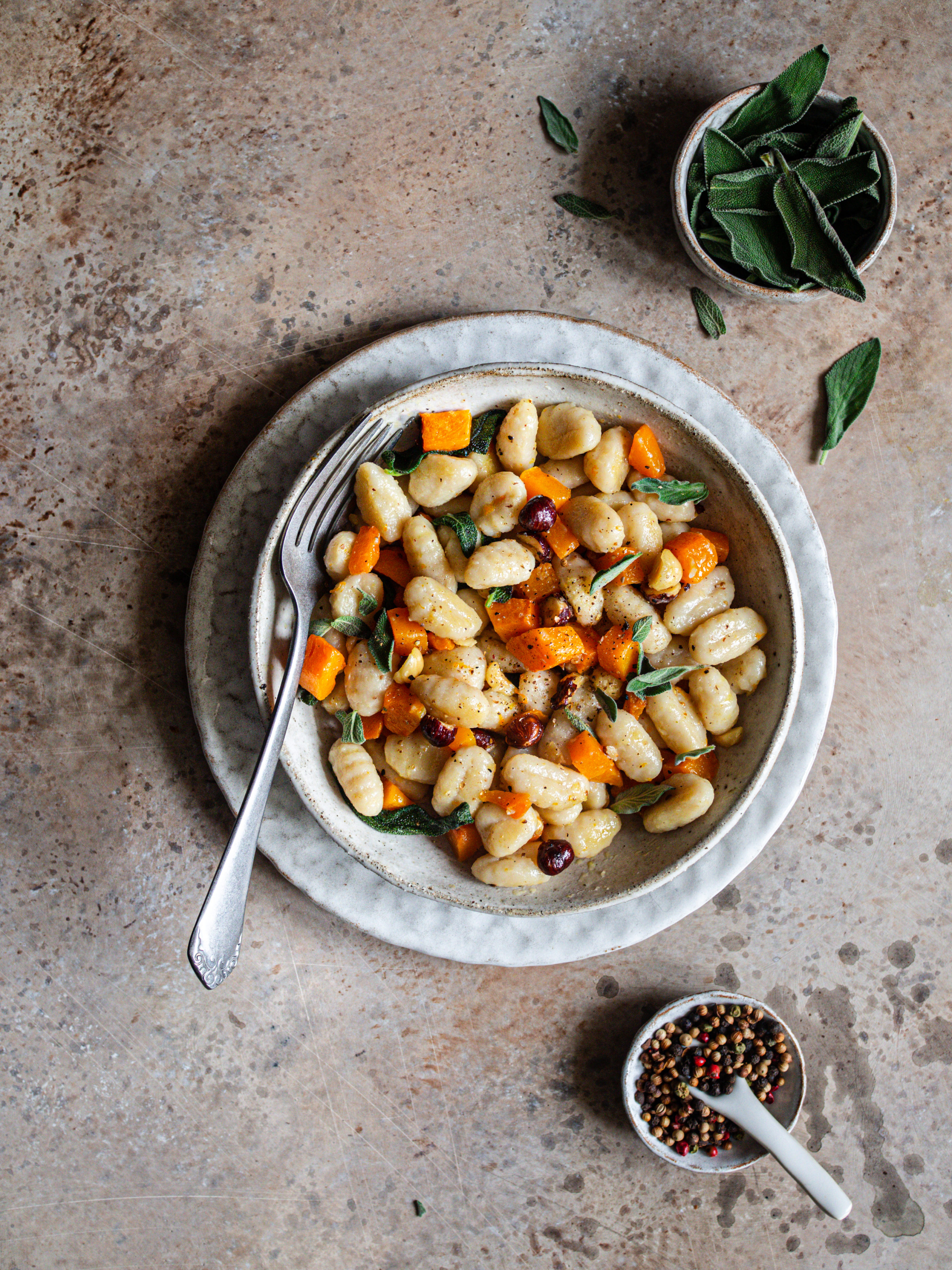 plan large de l'assiette de gnocchi au beurre de sauge et courge avec un pot de sauge fraîche et un pot de poivre