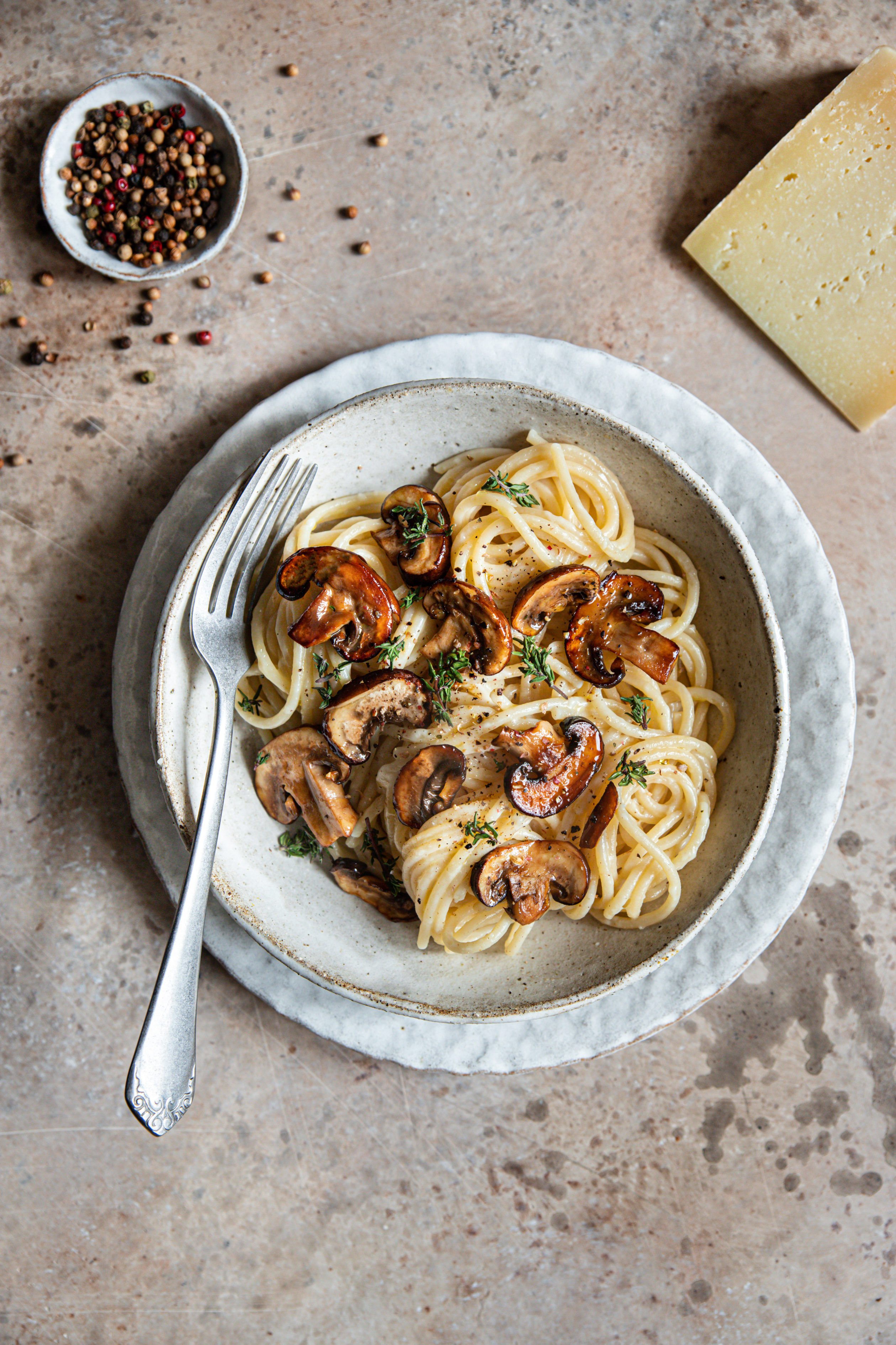 un bol de spaghetti au pecorino avec des champignons caramélisés sur le dessus et du thym frais