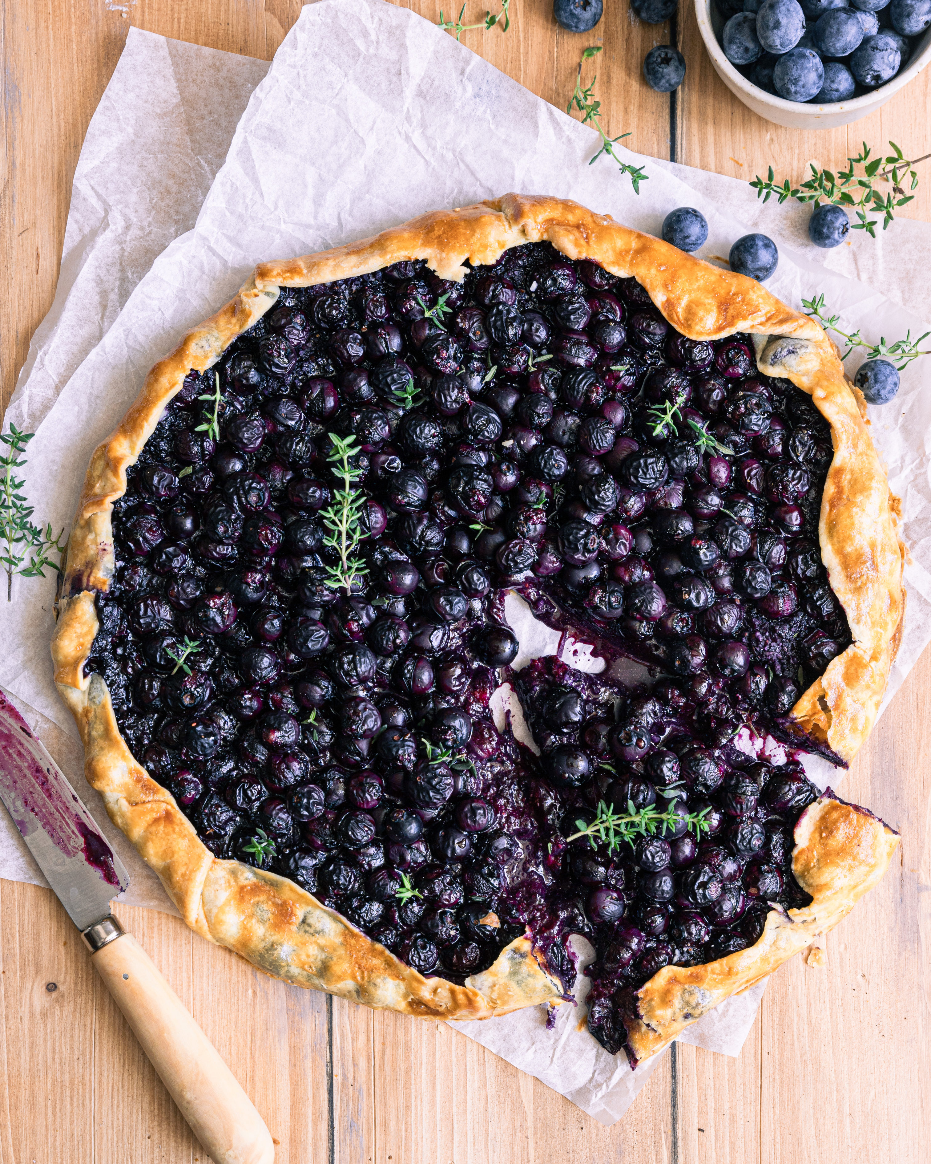 une tarte rustique aux myrtilles avec du thym sur une table en bois